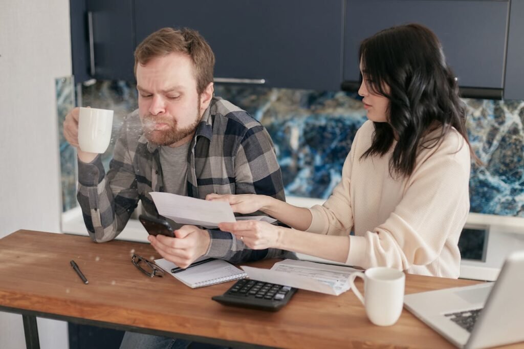Financial Inequality in Relationships How Money Impacts Mental Health and What to Do About It 3 Beawareofmecom A couple reviewing financial documents at a table with the man spitting out his coffee in shock while the woman points to something on the paper