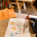 A young boy colors a Thanksgiving themed poster at a table highlighting how gentle parenting actually affects kids by encouraging creativity gratitude and emotional expression in a calm environment
