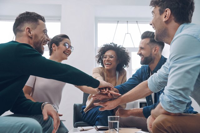 Confident young business team keeping hands clasped and smiling while sitting in the office together Beawareofmecom Supportive Work Environment